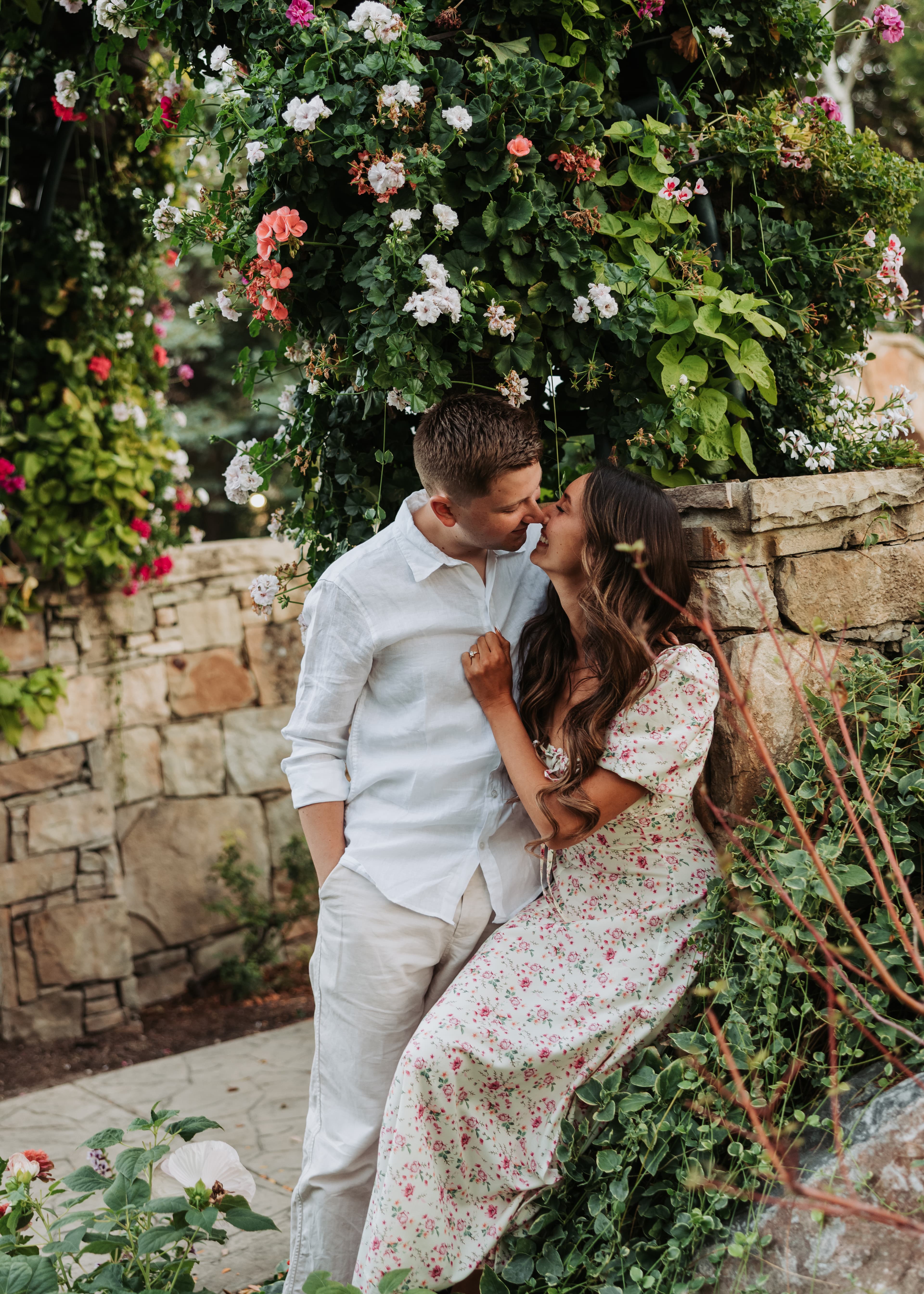 Bre and Bronson sharing a moment beside a flowering stone wall