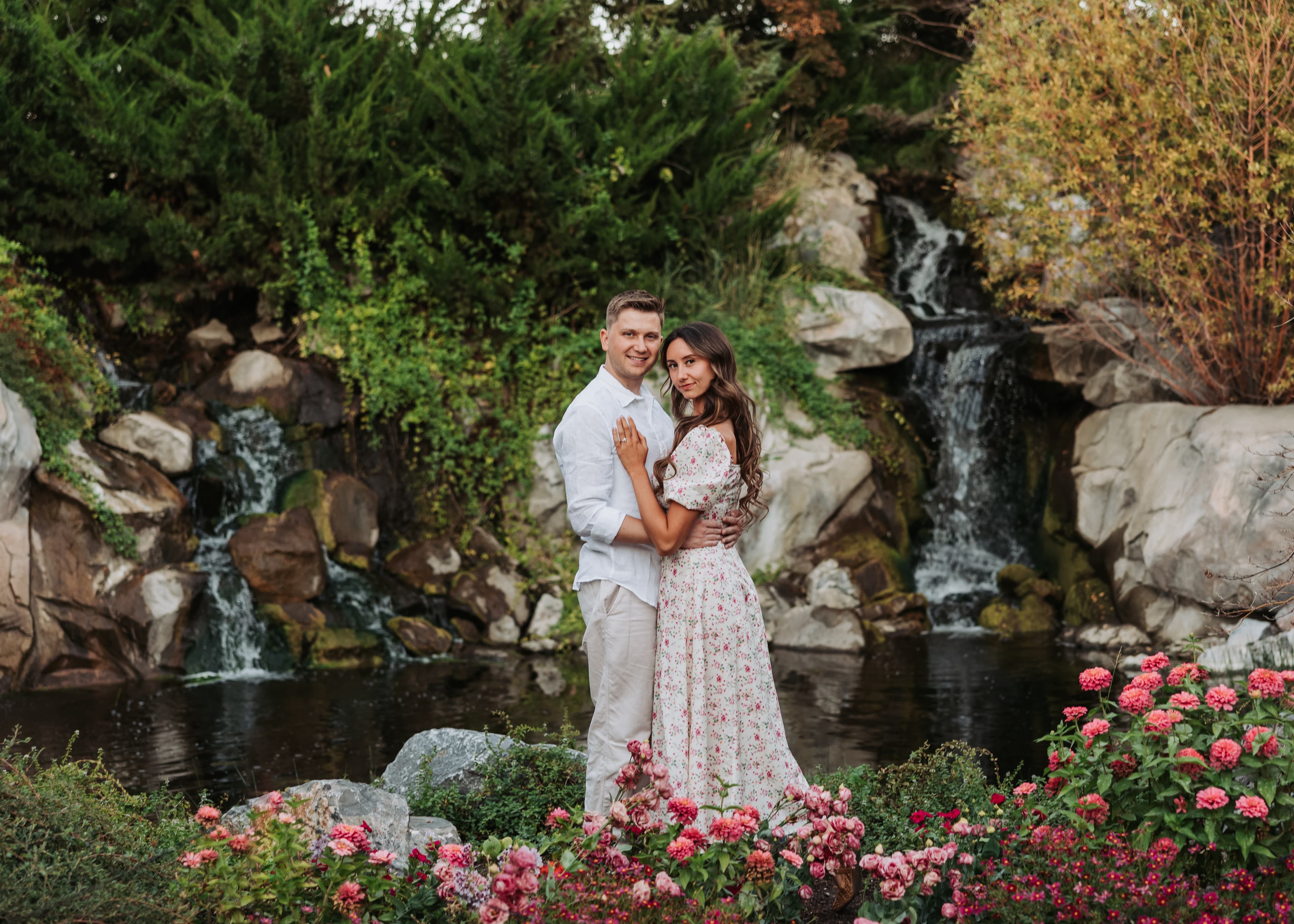 Bronson and Bre together beside a waterfall, surrounded by flowers and greenery.